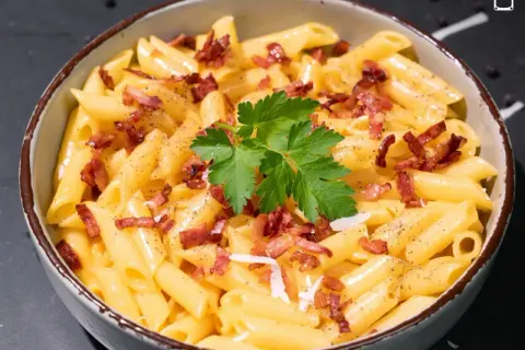 Un tazón de macarrones a la carbonara, cubiertos con trozos de tocino crujiente, perejil fresco y pimienta negra.