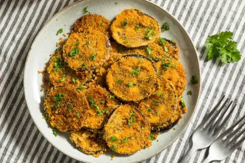Berenjenas rebozadas con harina y huevo, doradas y crujientes, espolvoreadas con perejil fresco. Un plato delicioso y fácil de preparar.