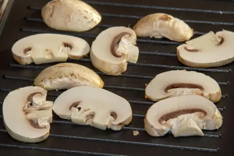 Champiñones cortados a la mitad y enteros sobre una parrilla, listos para deliciosas recetas con champiñones.