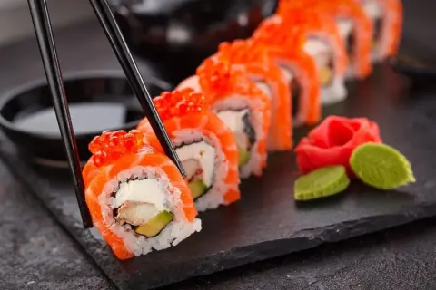 Palillos recogen un rollo de sushi con salmón y huevas de salmón, listo para disfrutar. Aprende como hacer sushi.