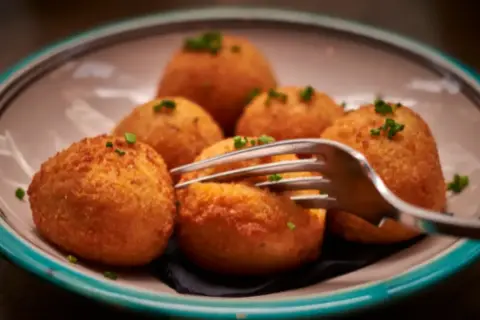 Croquetas de puchero doradas y crujientes, servidas en un plato con un tenedor listo para probarlas.