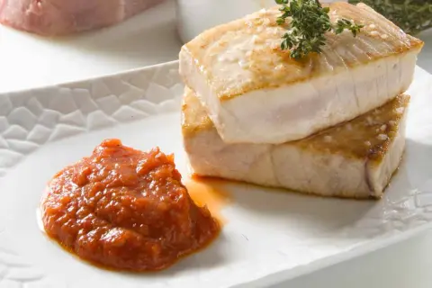 Dos jugosos trozos de atún a la plancha, con sal gruesa y una ramita de tomillo, acompañados de una porción de salsa de tomate casera.