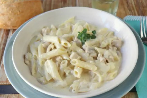 Un plato cremoso de macarrones con nata y trocitos de pollo, decorado con una ramita de tomillo.