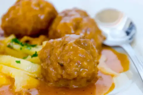 Albondigas a la jardinera, jugosas y cubiertas de salsa, acompañadas de patatas y perejil. Un plato casero listo para disfrutar.