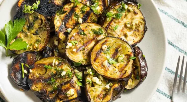 Rodajas de berenjenas a la plancha, doradas y tiernas, con ajo picado y perejil fresco. Un plato sencillo y delicioso.