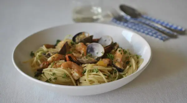 Un plato de spaghetti frutti di mare con gambas, mejillones y almejas, adornado con perejil fresco.