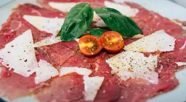Carpaccio de ternera con queso parmesano, hojas de albahaca y tomates cherry cortados por la mitad.