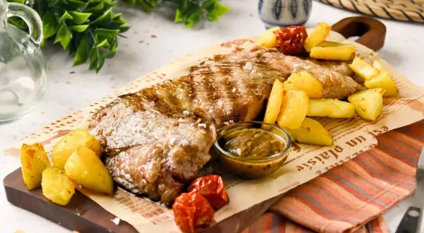 Jugosa carne al ajillo, servida con patatas rústicas y salsa, sobre papel de periódico. ¡Un festín para los sentidos!