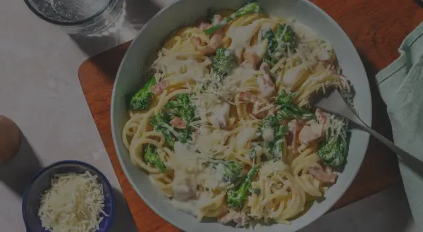 Un plato de pasta carbonara con huevo, brócoli y queso rallado, listo para disfrutar.