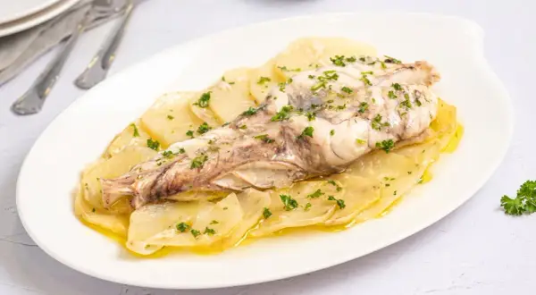 Rape al horno servido sobre patatas laminadas y espolvoreado con perejil fresco. Un plato sencillo y delicioso.