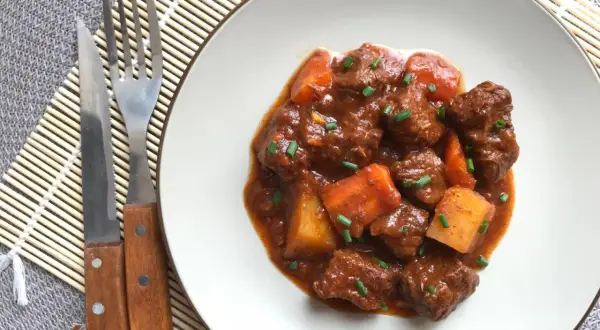 Un plato de goulash de ternera con trozos de patata y zanahoria, adornado con cebollino. Cubiertos de una rica salsa.