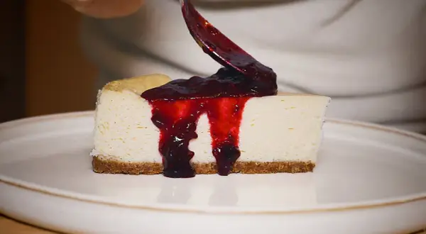Un trozo de new york cheesecake cremoso con salsa de frutos rojos cayendo.