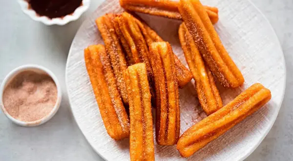 Churros sin gluten espolvoreados con azúcar y canela, servidos con chocolate caliente.