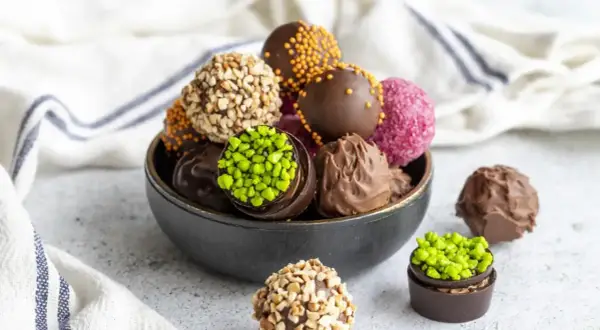 Un tazón lleno de deliciosas trufas de chocolate, algunas cubiertas de frutos secos, otras con chispas de colores y pistachos.