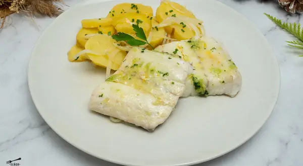 Dos filetes de merluza jugosos con patatas y cebolla, decorado con perejil fresco. Un plato delicioso y saludable.