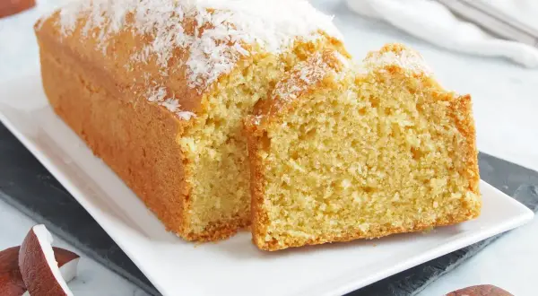Bizcocho de coco esponjoso, cubierto con coco rallado, servido en una bandeja blanca.