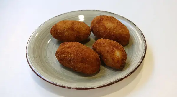 Cuatro croquetas de pollo de la abuela doradas y crujientes en un plato.