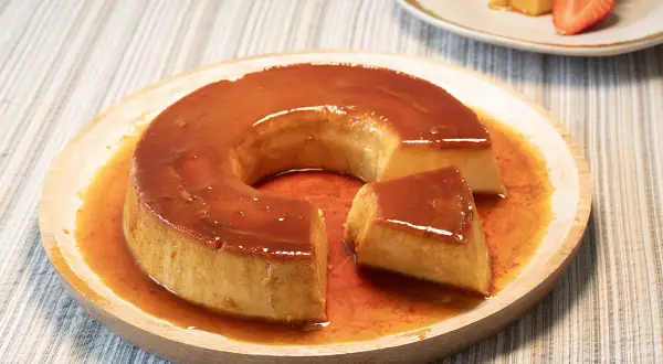 Un delicioso flan de leche condensada con caramelo líquido, servido en plato de madera.