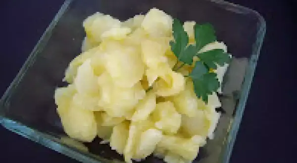Un cuenco de cristal contiene patatas al montón, un plato sencillo y reconfortante, adornado con una ramita de perejil fresco.