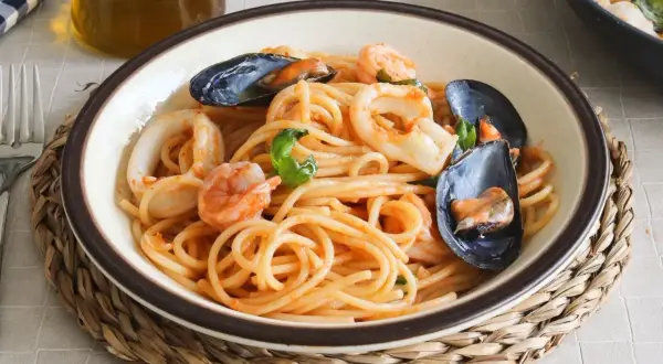 Un plato de espaguetis a la marinera con gambas, calamares y mejillones, servido en un cuenco sobre una esterilla de mimbre.