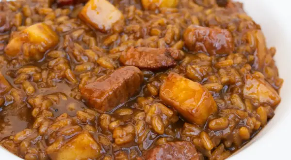 Un plato de arroz con acelgas y trozos de carne en una salsa oscura y apetitosa.