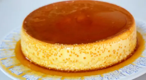 Delicioso flan de queso Philadelphia con caramelo líquido, servido en un plato blanco con diseño azul.