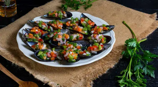 Mejillones a la vinagreta, frescos y coloridos, servidos en una concha con picadillo de verduras.
