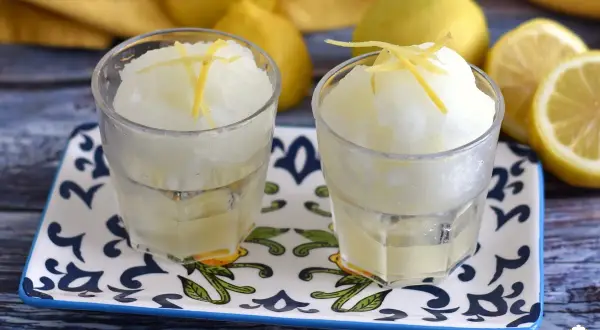 Dos vasos de refrescante helado de limón, adornados con ralladura de limón, sobre una bandeja decorada.