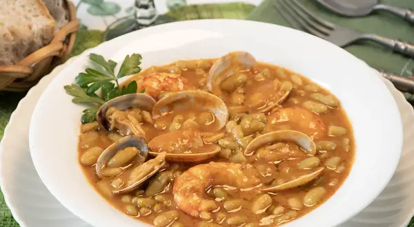 Plato de verdinas con almejas y gambas, decorado con perejil. Acompañado de pan en cesta.