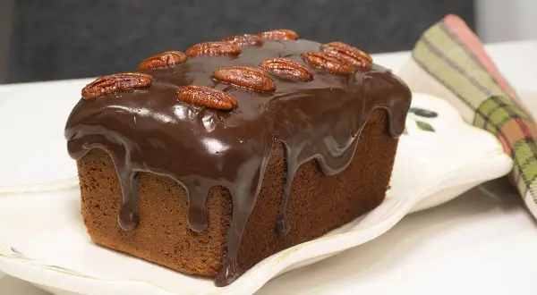 Bizcocho de platano y chocolate cubierto de glaseado y nueces pecanas, listo para disfrutar.