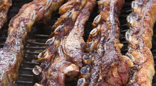 Costillas de churrasco a la plancha, doradas y jugosas, cocinándose lentamente sobre la parrilla.