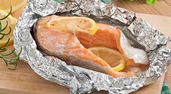 Salmón jugoso en papel de aluminio con rodajas de limón y romero.