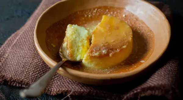 Un trozo de flan de yogur cremoso, bañado en caramelo líquido, servido en un cuenco de barro.