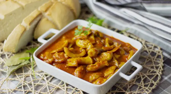 Deliciosa jibia en salsa, servida en un cuenco blanco, acompañada de pan rústico y hojas de laurel.