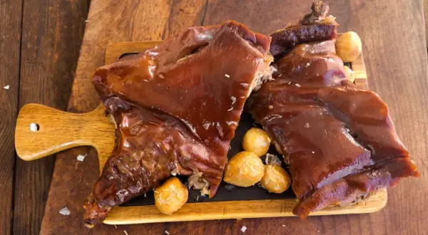 Delicioso cochinillo al horno, crujiente y jugoso, servido con patatas asadas.