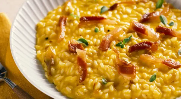 Cremoso risotto de queso, con trozos de panceta crujiente y hojas verdes.