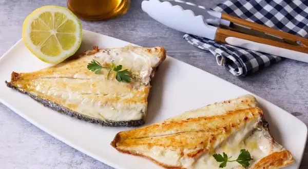 Dos filetes de dorada a la plancha, jugosos y dorados, servidos con perejil fresco y una rodaja de limón.