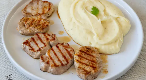 Cinco medallones de solomillo a la parrilla con puré de patatas cremoso, decorado con una ramita de perejil.