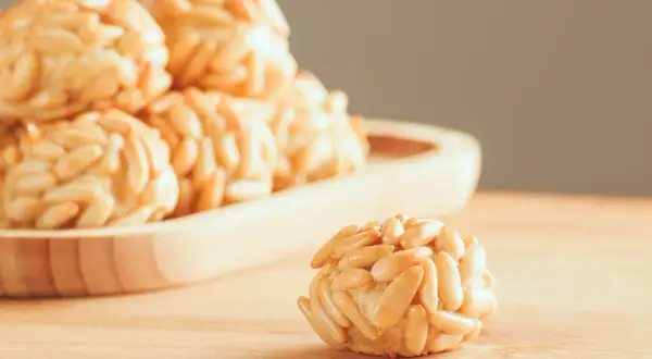 Rosquillas de naranja cubiertas de piñones, con un dulce aroma cítrico y un crujiente exterior.