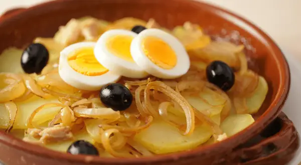 Bacalao a la portuguesa con patatas, cebolla, aceitunas negras y huevos duros en cazuela de barro.