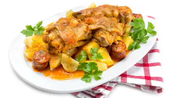 Manitas de cerdo receta tradicional de la abuela, con patatas y chorizo, servido en plato blanco con perejil fresco.