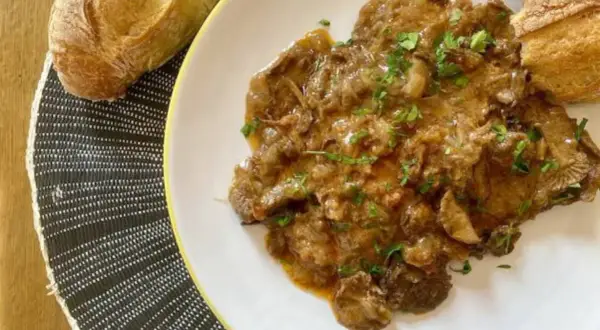 Plato de fricando de ternera con salsa cremosa y trozos de pan crujiente.