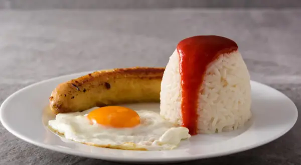 Un plato de arroz a la cubana con huevo frito y salchicha, cubierto con salsa de tomate.