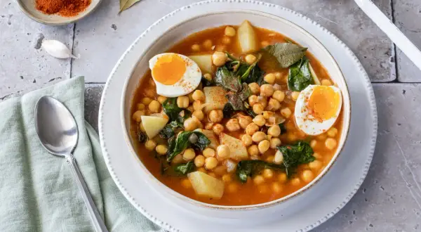Un reconfortante plato de garbanzos con espinacas, patatas y huevos cocidos, espolvoreado con pimentón.