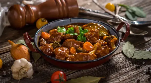 Caldereta de cordero humeante, con trozos de carne tierna, zanahoria y brócoli, servida en una cazuela rústica.