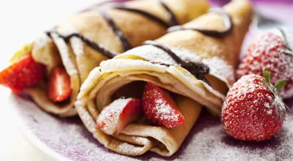 Deliciosos crepes sin huevo rellenos de fresas y bañados en chocolate, espolvoreados con azúcar glas.