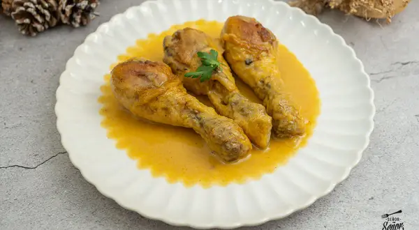 Tres jamoncitos de pollo dorados en una salsa cremosa, servidos en un plato blanco con un toque de perejil.