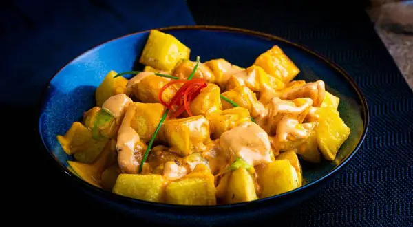 Patatas bravas receta: trozos dorados de patata cubiertos con una cremosa salsa rosada y decorados con pimiento rojo y cebollino.