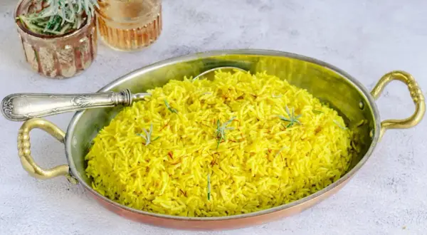 Un aromático arroz al curry, teñido de un vibrante amarillo por la cúrcuma y decorado con hebras de azafrán y romero fresco.