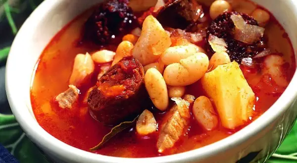 Un reconfortante plato de alubias con chorizo, trozos de morcilla y patatas en un cuenco blanco.